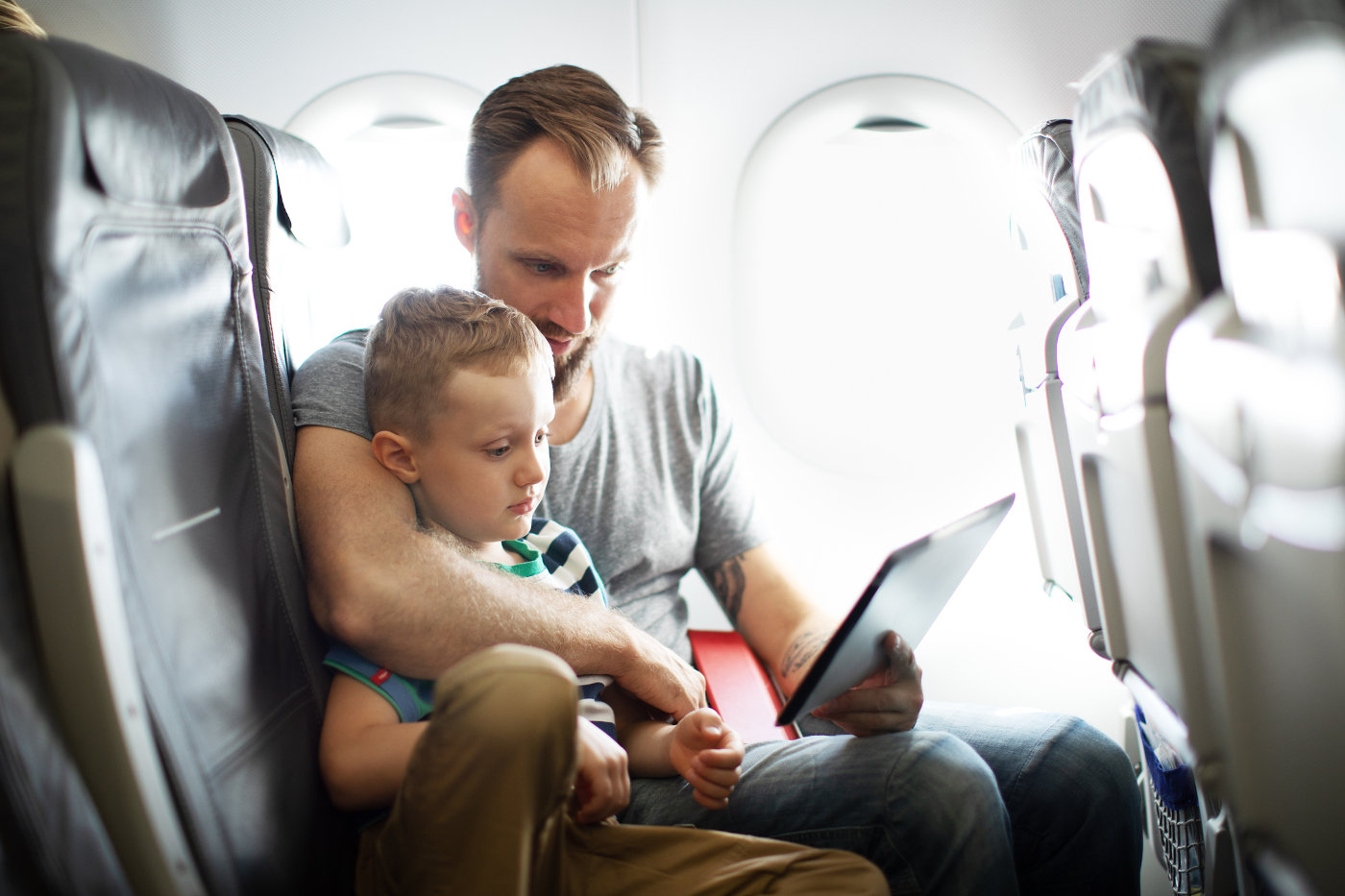 Vater mit Sohn im Flugzeug schauen etwas auf dem Tablet