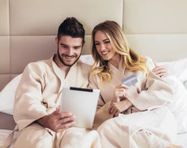 Junges Paar in einem Bett eines Luxushotels beim Online-Shopping mit Kreditkarte